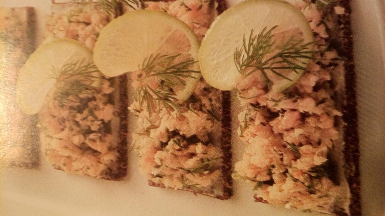 Kanapki z pastą rybną na ciemnym pieczywie, udekorowane plasterkiem cytryny i gałązką koperku.