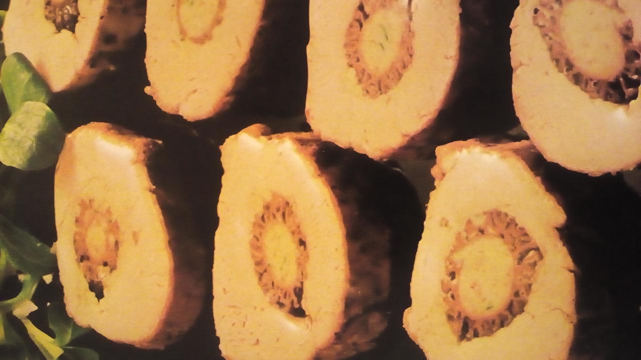 Plastry roladki mięsnej z nadzieniem, ułożone na ciemnym tle z zielonymi listkami.