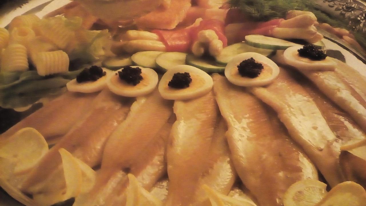 Śledzie w oleju z jajkiem przepiórczym i kawiorem, dekorowane cytryną i ogórkiem, na srebrnej tacy, element cateringu świątecznego.