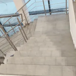 Schody wyłożone szarymi płytkami, z metalową balustradą i przeszklonym sufitem, widok z góry.