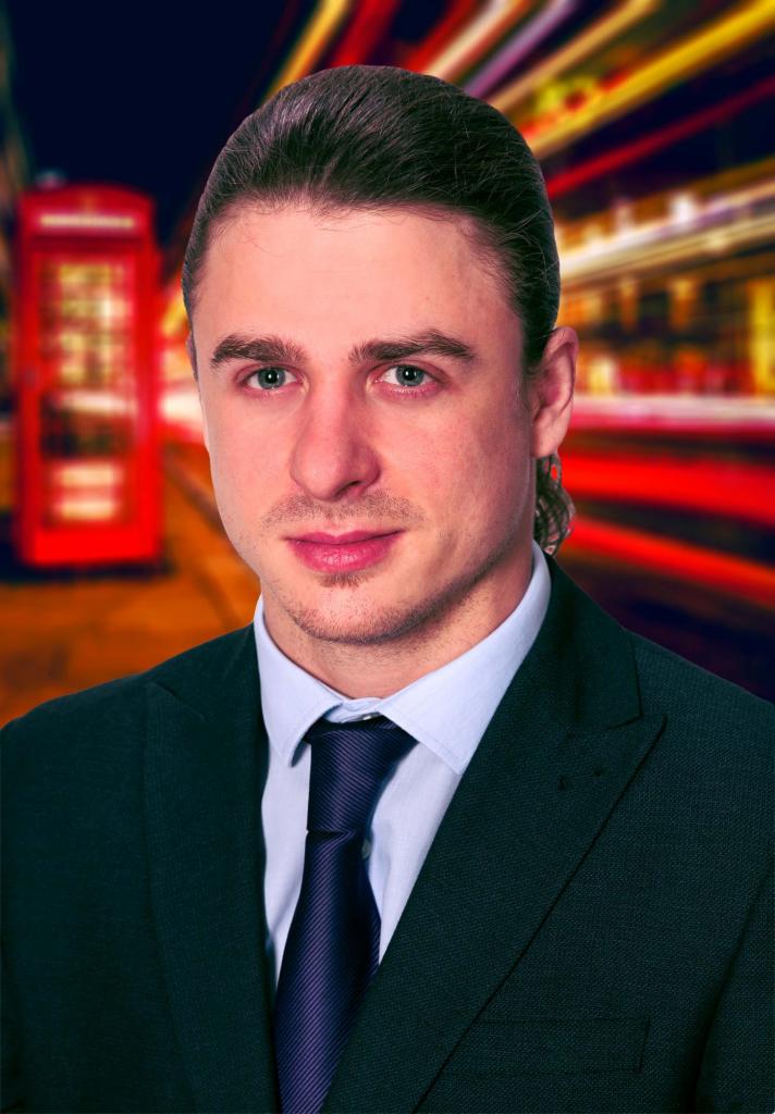 Portret mężczyzny w garniturze na rozmytym tle londyńskiej ulicy z charakterystyczną czerwoną budką telefoniczną.