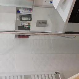 Szklana kabina prysznicowa z chromowanymi profilami, białe płytki z geometrycznym wzorem, czarna szafka pod umywalką i żółty ręcznik w nowoczesnej łazience.