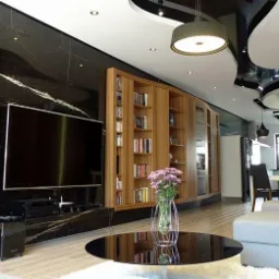 Elegancki salon z czarną marmurową ścianą, drewnianymi regałami na książki, dużym telewizorem i okrągłym stolikiem kawowym z bukietem kwiatów; sufit z podwieszanymi elementami i nowoczesnym...