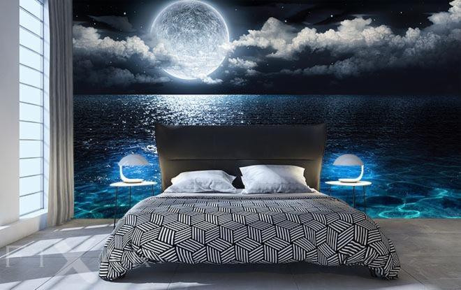 Sypialnia z fototapetą przedstawiającą nocny krajobraz morski z księżycem w pełni, oświetlona lampkami nocnymi na okrągłych stolikach.