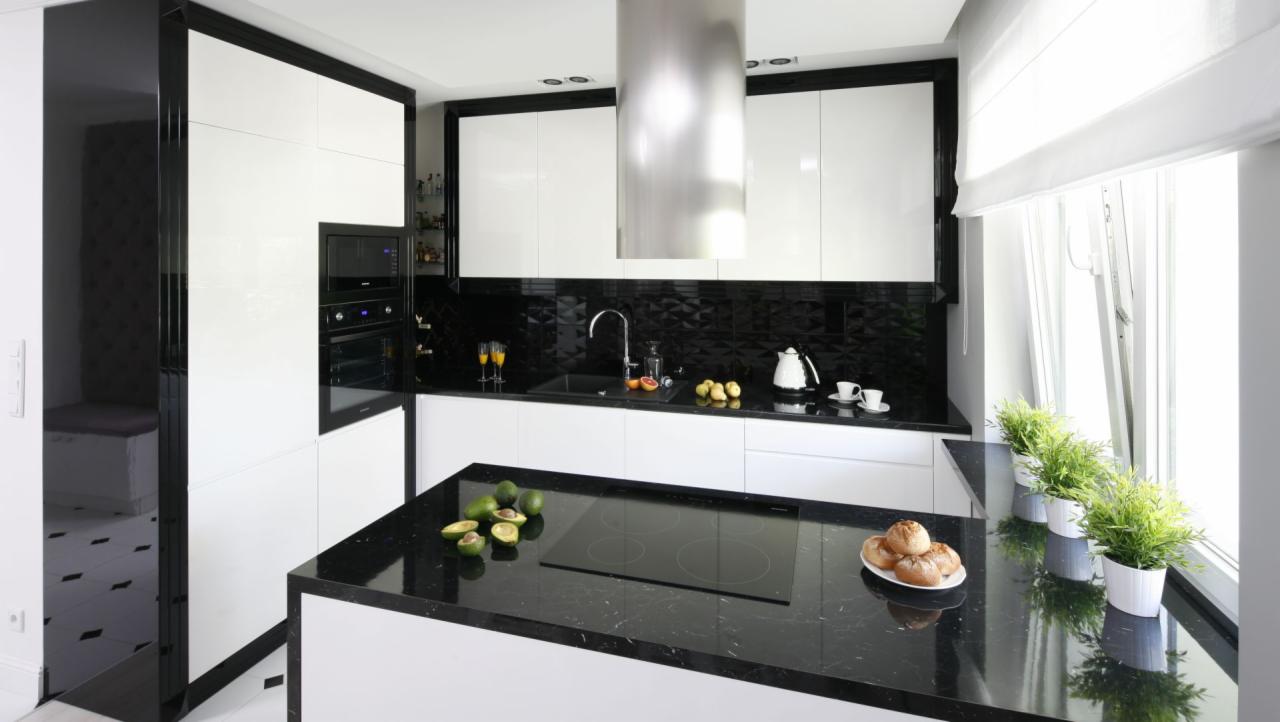 Nowoczesna kuchnia z biało-czarnymi szafkami, czarnym blatem z awokado i bułkami na wyspie, oraz roślinami doniczkowymi przy oknie.