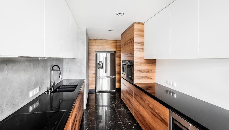 Nowoczesna kuchnia z czarną marmurową podłogą, drewnianymi i białymi szafkami, oraz stalową lodówką dwudrzwiową.