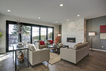 Nowoczesny salon z przesuwnymi drzwiami balkonowymi w czarnej ramie, marmurowym kominkiem i parkietem w odcieniach brązu. Dwa beżowe fotele z czerwonymi poduszkami i dwie sofy ustawione wokół...