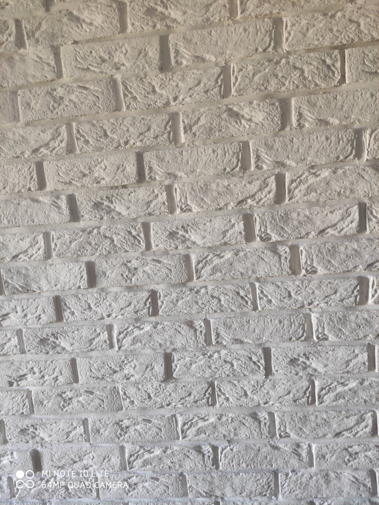 Biała ściana z dekoracyjnej cegły, nierówna faktura, widoczne fugi, oświetlenie od góry, imitacja starego muru.