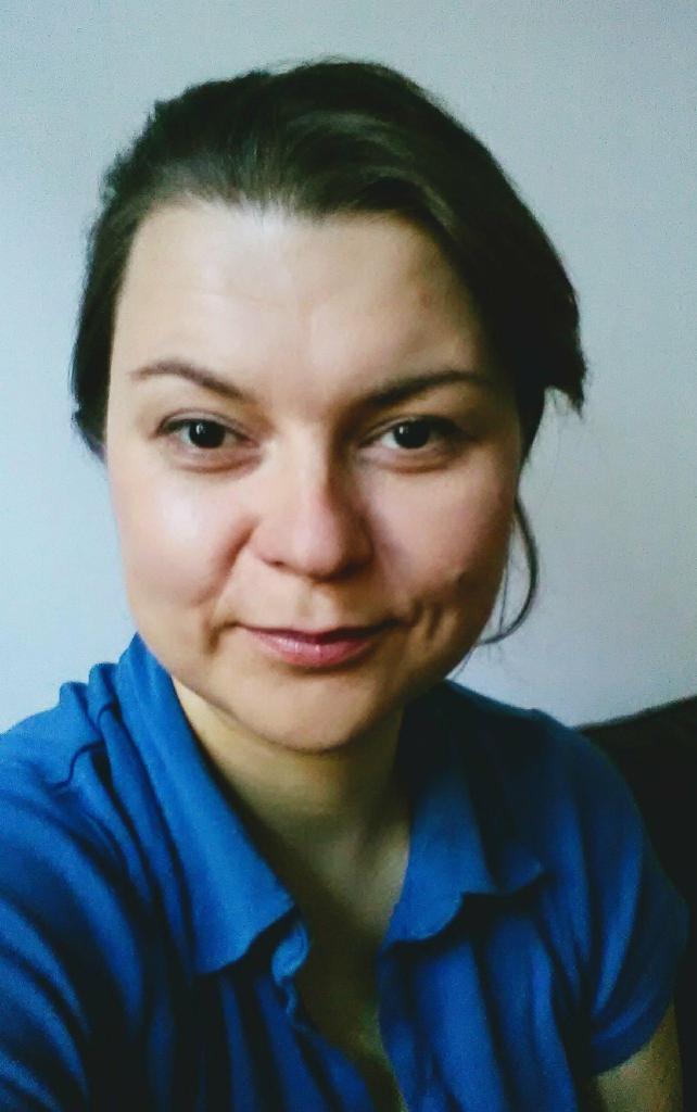 Portret uśmiechniętej kobiety w niebieskiej koszuli, potencjalnie logopedy, z widocznymi dołeczkami na policzkach.