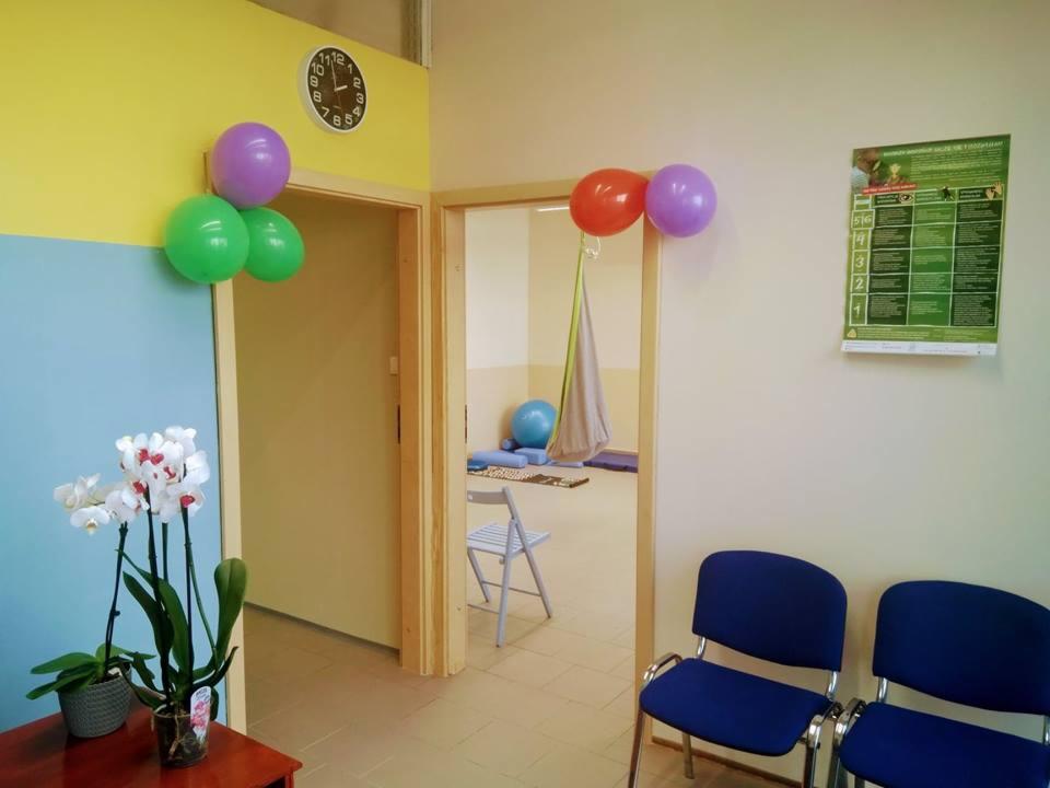 Gabinet z krzesłami, piłką rehabilitacyjną, huśtawką terapeutyczną i dekoracjami z balonów.