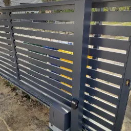 Szara, przesuwna brama z poziomymi panelami i wbudowanym oświetleniem LED na słupku, widoczny napęd bramy i elementy mechaniczne montażu.