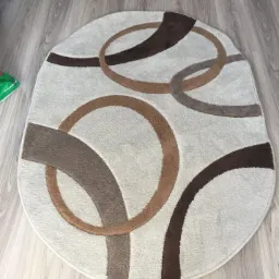 Owalny dywan z kremowym tłem i abstrakcyjnym wzorem z brązowych okręgów na podłodze z paneli.