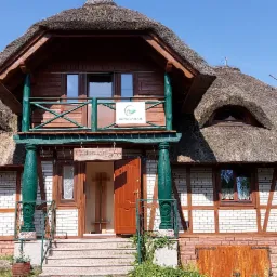 Budynek z białej cegły z drewnianymi elementami i strzechą, na balkonie logo z napisem 'ODPOCZNIENIE'.