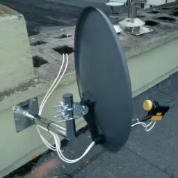 Szara antena satelitarna z konwerterem unicable zamontowana na dachu w Gdyni, przymocowana do komina za pomocą metalowych uchwytów.