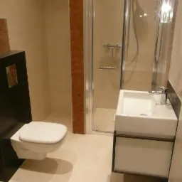 Nowoczesna łazienka z podwieszaną toaletą w czarnej obudowie, kabiną prysznicową ze srebrnymi ramami i białą umywalką nablatową z szafką.