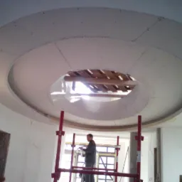 Montaż okrągłego sufitu podwieszanego z płyty gipsowo-kartonowej, widoczny pracownik na rusztowaniu i otwór w suficie.