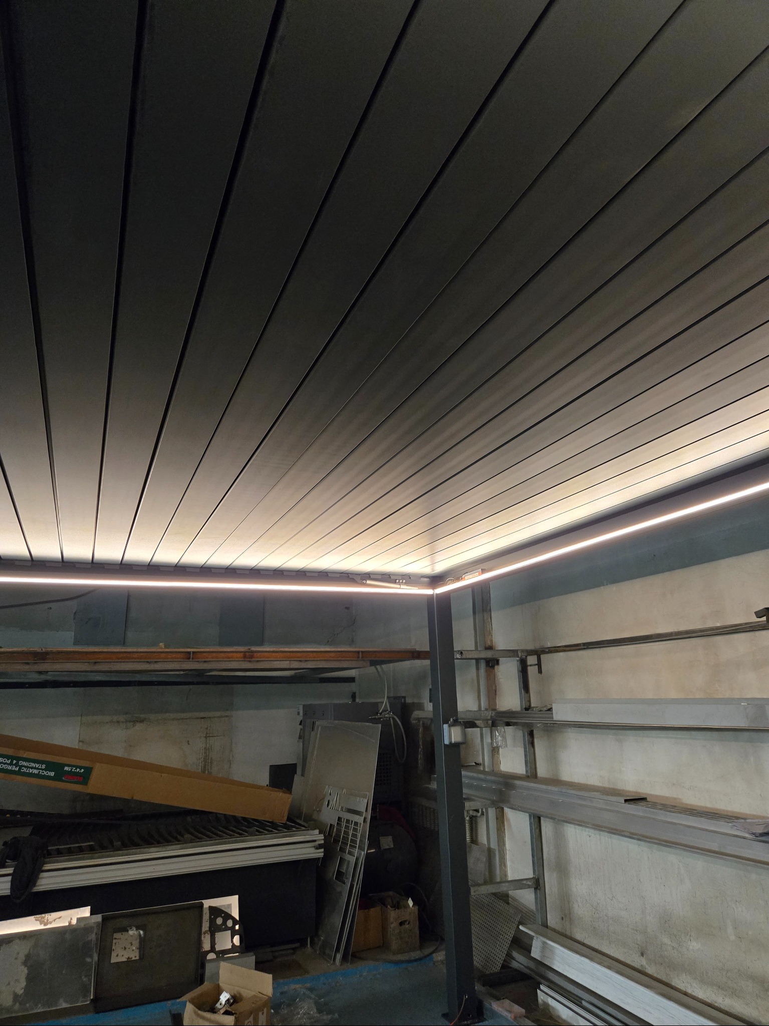 Metalowa pergola z oświetleniem LED, widok od dołu. Elementy konstrukcyjne i materiały w tle. Ukośne ułożenie paneli.