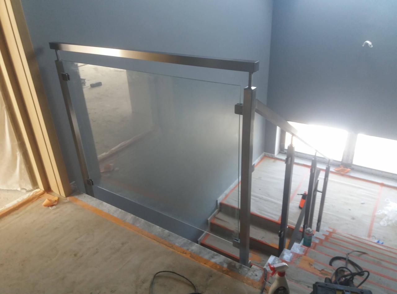 Szklana balustrada schodowa z metalowymi elementami w kolorze grafitowym, widok z góry na schody w trakcie prac wykończeniowych.