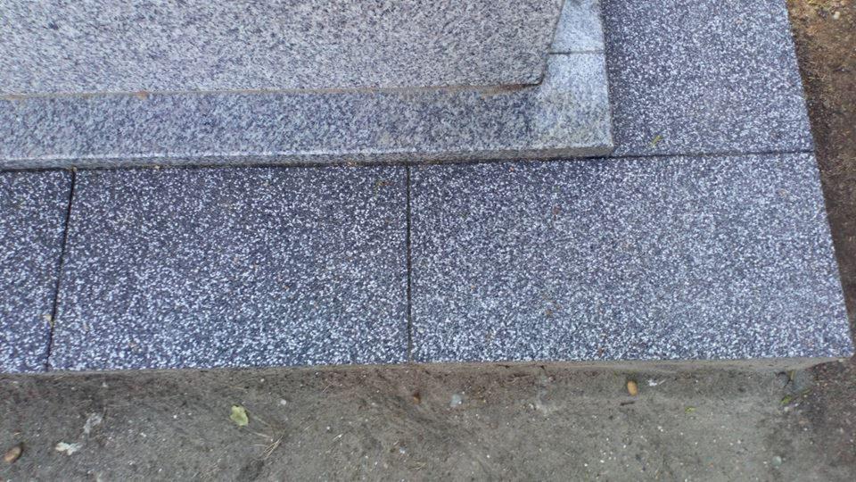 Ułożona, ciemnoszara kostka granitowa z jasnymi plamkami, przylegająca do szarej, gruboziarnistej płyty granitowej z widoczną krawędzią