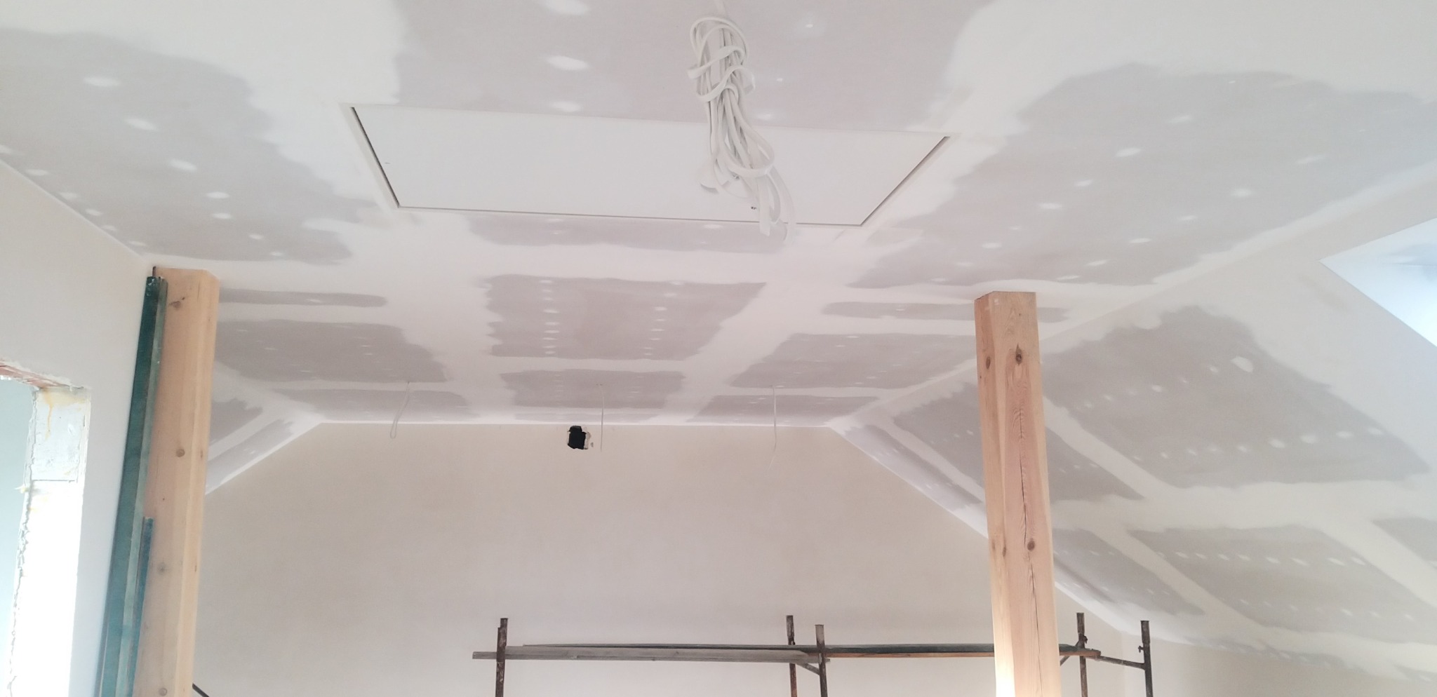 Skośny sufit poddasza po montażu płyt gipsowo-kartonowych, widoczne łączenia przygotowane do szpachlowania. Podpory drewniane i fragment rusztowania.