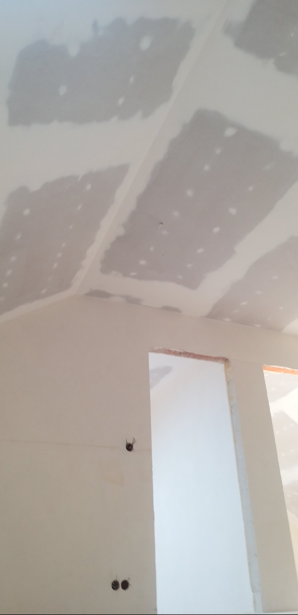 Sufit poddasza po szpachlowaniu płyt gipsowo-kartonowych, widoczne łączenia i miejsca po wkrętach. Ściana z widocznymi puszkami elektrycznymi i otworem drzwiowym.