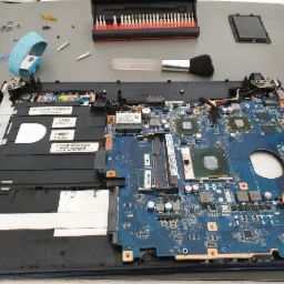 Otwarty laptop Sony z widoczną płytą główną, narzędziami do naprawy, pędzelkiem, opaską antystatyczną i zestawem wkrętaków na szarym stole.