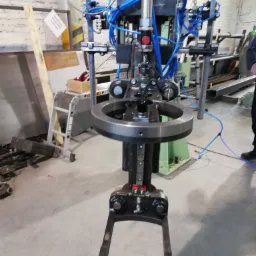 Detale pneumatycznego urządzenia do montażu elementów bram, widoczne niebieskie przewody i metalowa konstrukcja w warsztacie.