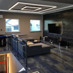 Nowoczesny salon z podwieszanym sufitem z oświetleniem LED, szarą sofą modułową, stołem bilardowym i ciemną ścianą z telewizorem.