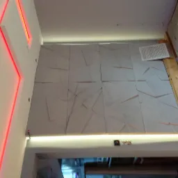 Ściana pokryta dekoracyjnymi panelami 3D w trakcie montażu, widoczne drewniane elementy konstrukcyjne, górna krawędź podświetlona listwą LED, obok fragment ściany z pionową, czerwoną linią świetlną.