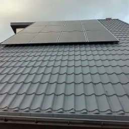 Szary dach z blachodachówki z zamontowanymi panelami fotowoltaicznymi w pochmurny dzień.