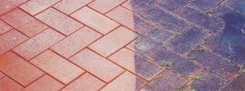 Częściowo wyczyszczona kostka brukowa, z widocznym kontrastem między czystą, czerwoną powierzchnią a brudną, ciemną częścią z chwastami w spoinach.