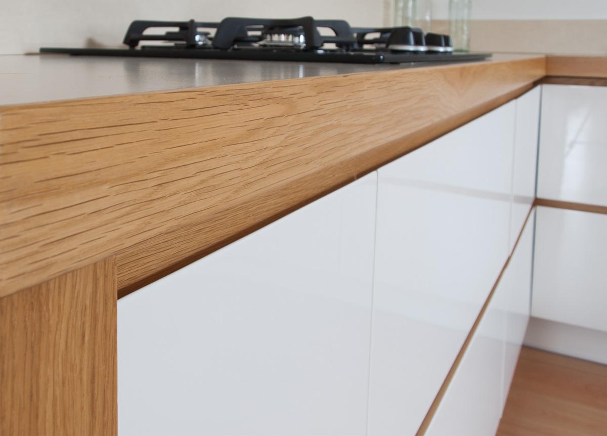 Fragment białej, lakierowanej zabudowy kuchennej z drewnianym blatem i wykończeniem, widoczna płyta gazowa.