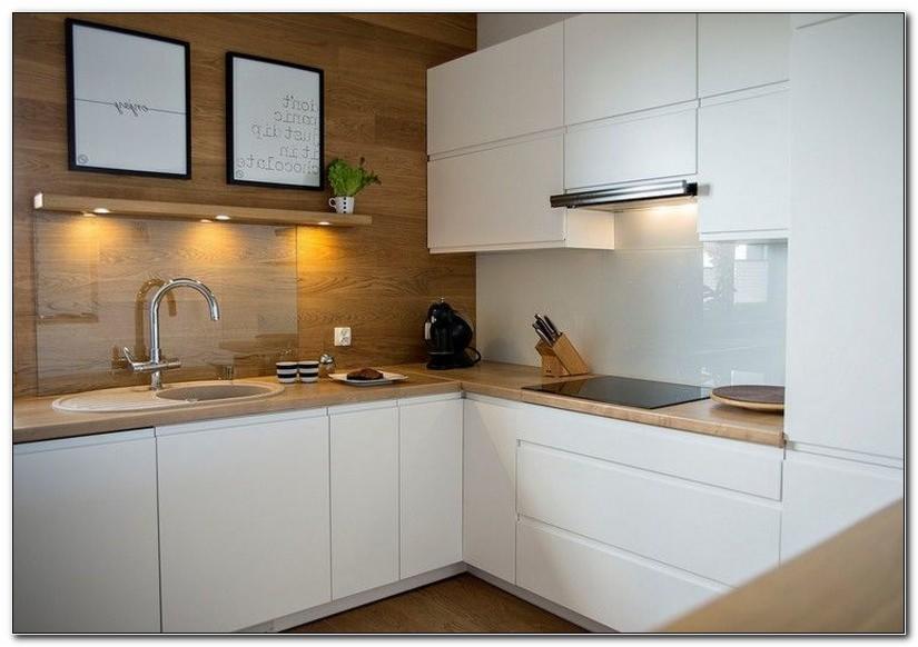 Nowoczesna, jasna kuchnia z białymi frontami szafek i blatem z jasnego drewna. Na blacie widoczny zlew z chromowaną baterią, płyta indukcyjna, ekspres do kawy i akcesoria kuchenne. Ściana...