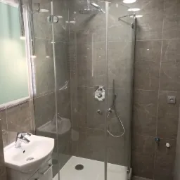 Nowoczesna łazienka z kabiną prysznicową narożną, marmurowe płytki, umywalka z szafką i designerskie oświetlenie punktowe.