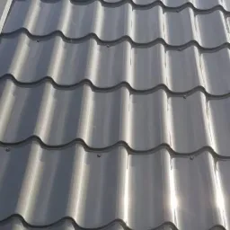 Błyszczące, grafitowe pokrycie dachowe z blachy trapezowej, widoczne mocowania, fragment obróbki blacharskiej przy krawędzi dachu.