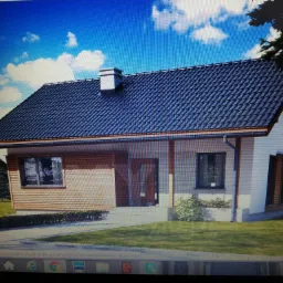 Wizualizacja parterowego domu jednorodzinnego z ciemną dachówką, drewnianą elewacją i brukowanym podjazdem, widok z poziomu trawnika w słoneczny dzień.