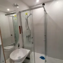 Nowoczesna łazienka z kabiną prysznicową z przesuwnymi drzwiami, owalną umywalką nablatową i dużym okrągłym lustrem, widoczne zabezpieczenia folią na brodziku.