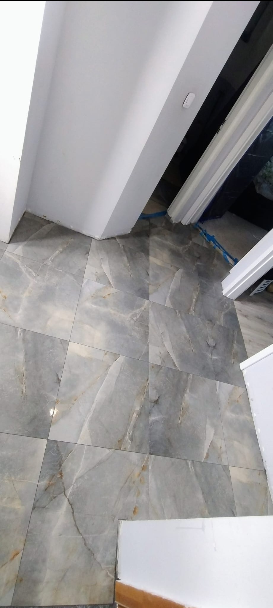 Ułożone, szare płytki podłogowe z marmurkowym wzorem, widok z góry, fragment białego sufitu i listwy przypodłogowe. Układanie płytek z dbałością o detale.