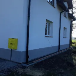 Elewacja domu jednorodzinnego po remoncie, z widocznym gazomierzem i nową instalacją odprowadzającą wodę deszczową.
