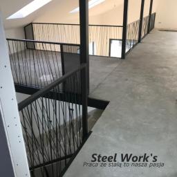 Steel-works Piotr Kowalczyk - Wnętrze poddasza z czarnymi, stalowymi balustradami o minimalistycznym designie, widok z góry na schody i korytarz, logo firmy na posadzce.