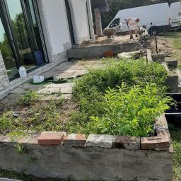 Usługi remontowo- budowlane Przemysław Bąk - Przygotowanie terenu pod ogród przed domem z białymi ścianami i dużymi oknami, widoczny pracownik z łopatą i biały samochód dostawczy w tle.
