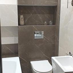 Usługi remontowo- budowlane Przemysław Bąk - Nowoczesna łazienka z brązowo-białymi płytkami imitującymi marmur, wisząca toaleta, umywalka na postumencie i wnęka w ścianie z dekoracjami.