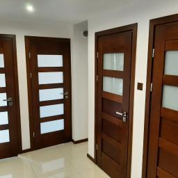 Usługi remontowo- budowlane Przemysław Bąk - Trzy ciemnobrązowe drzwi wewnętrzne z matowymi szybami w jasnym korytarzu z błyszczącą podłogą.