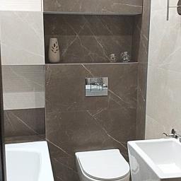 Usługi remontowo- budowlane Przemysław Bąk - Nowoczesna łazienka z marmurowymi płytkami w odcieniach szarości i beżu, wisząca toaleta, umywalka na postumencie i wanna, oświetlenie punktowe oraz dekoracyjne akcesoria w niszy.