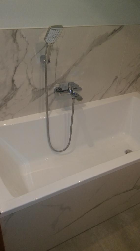 Biała wanna z armaturą i marmurową okładziną ścienną, widok z góry.