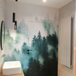 Nowoczesna łazienka z umywalką nablatową, lustrem i fototapetą z motywem mglistego lasu, drzwi ukryte w fototapecie, oświetlenie punktowe.