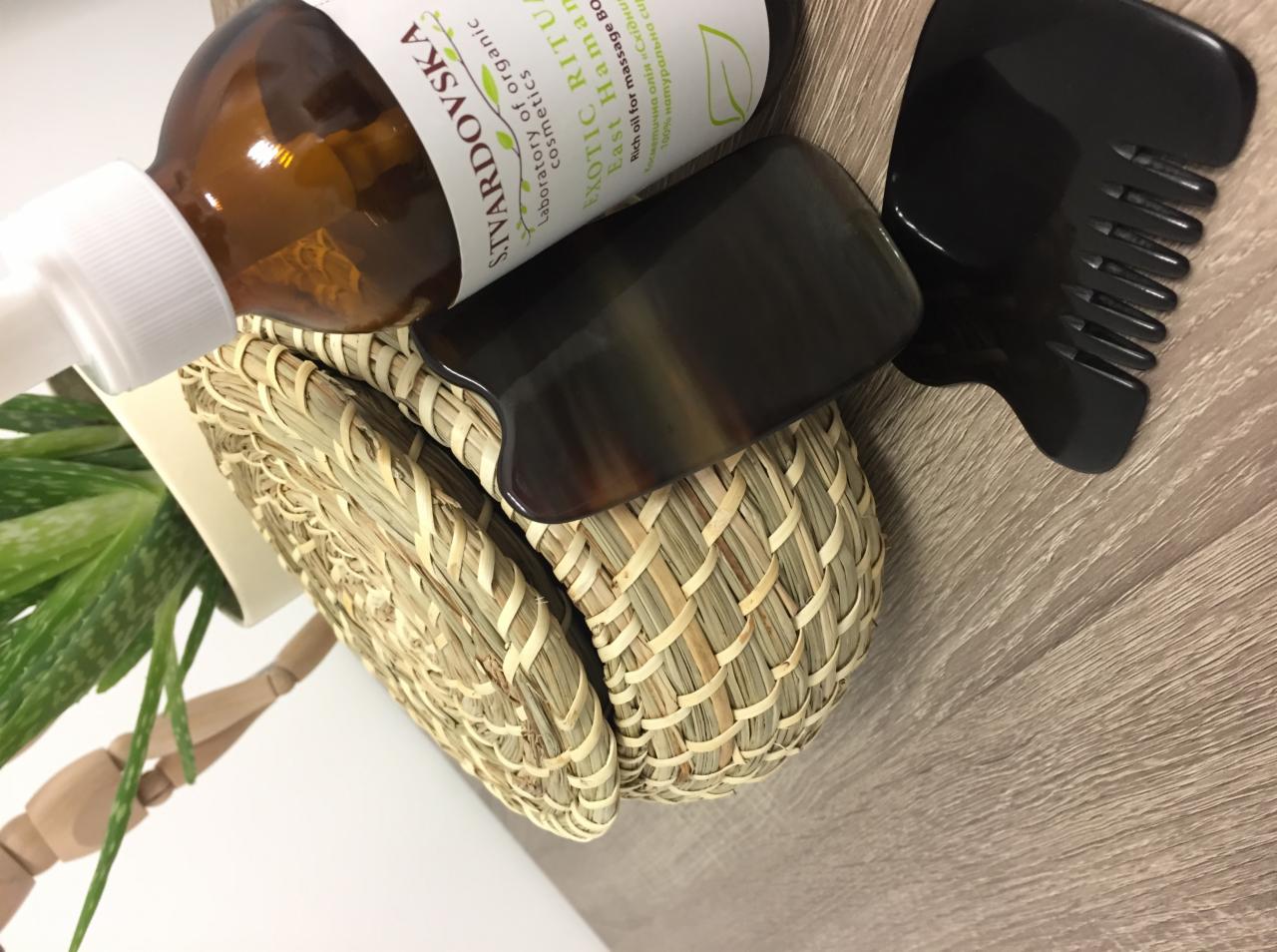 Zestaw do masażu Gua Sha z Poznania: kamień Gua Sha z rogu, grzebień do masażu i olejek na plecionym koszyczku na drewnianym tle.