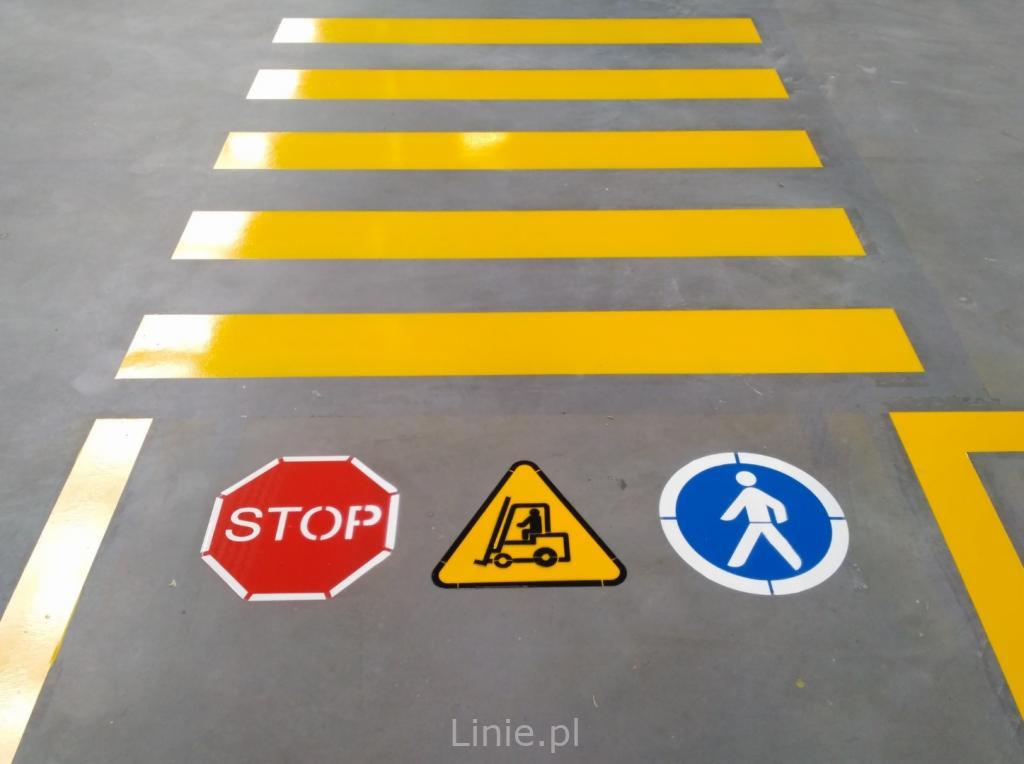 Żółte pasy przejścia dla pieszych na szarym betonowym podłożu, uzupełnione o znaki ostrzegawcze STOP, uwaga na wózki widłowe i przejście dla pieszych, z widocznym połyskiem świeżo nałożonej farby.