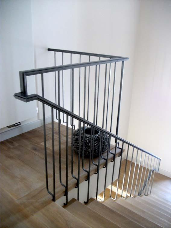 Metalowa balustrada schodowa z pionowymi prętami, drewniane stopnie schodów, dekoracyjny koszyk na podeście, minimalistyczny design.