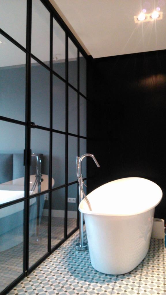 Nowoczesna łazienka z wanną wolnostojącą i przeszkloną ścianą z czarnymi szprosami, wzorzysta podłoga.